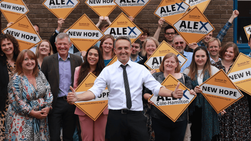 Scottish Liberal Democrats leader Alex Cole-Hamilton stood amongst a legion of supporters in the background holding up orange supportive placards.
