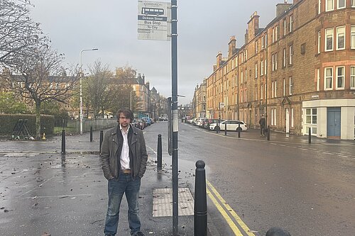 Jack Caldwell standing under a bus stop sign on Dalmeny Street